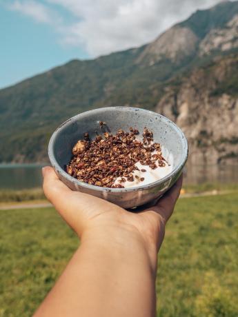 Crunchy chocolate muesli with yogurt in bowl in front of mountain and lake.